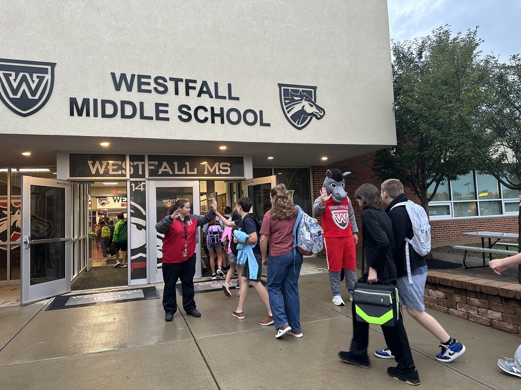 Students coming into the front of school building being greeted by Marty the Mustang