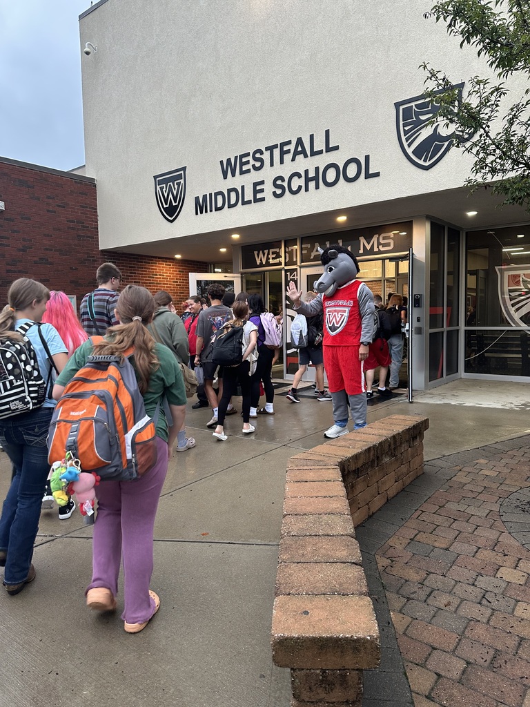Students coming into the front of school building being greeted by Marty the Mustang