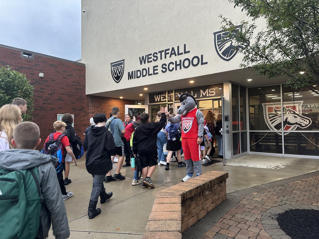 Students coming into the front of school building being greeted by Marty the Mustang