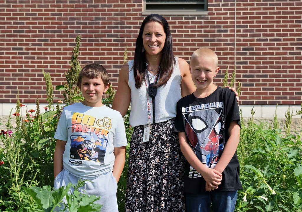 Teacher standing with two students in a garden