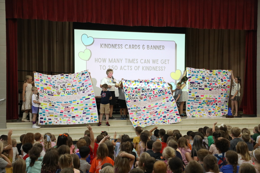 Students holding up three banners covered in colorful pieces of tape - Banner reads Be Kind Stick Together