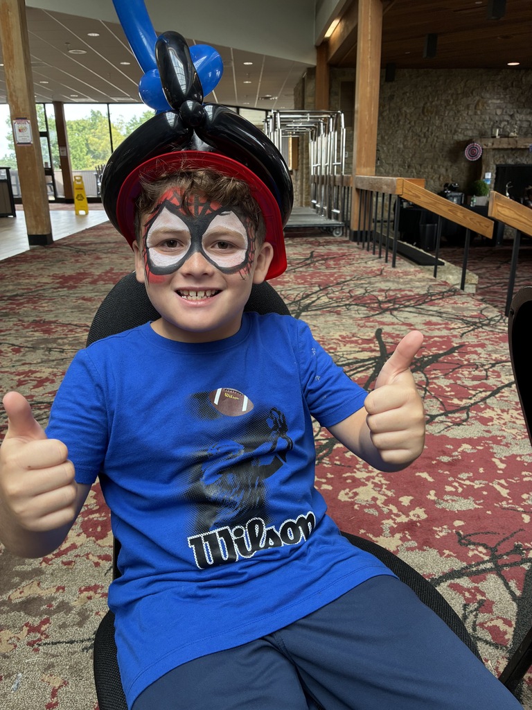 Student with face painted holding up double thumbs up