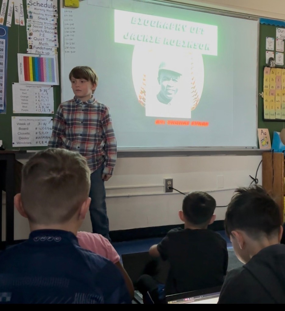 Student presents biography in front of classmates and small group of parents.