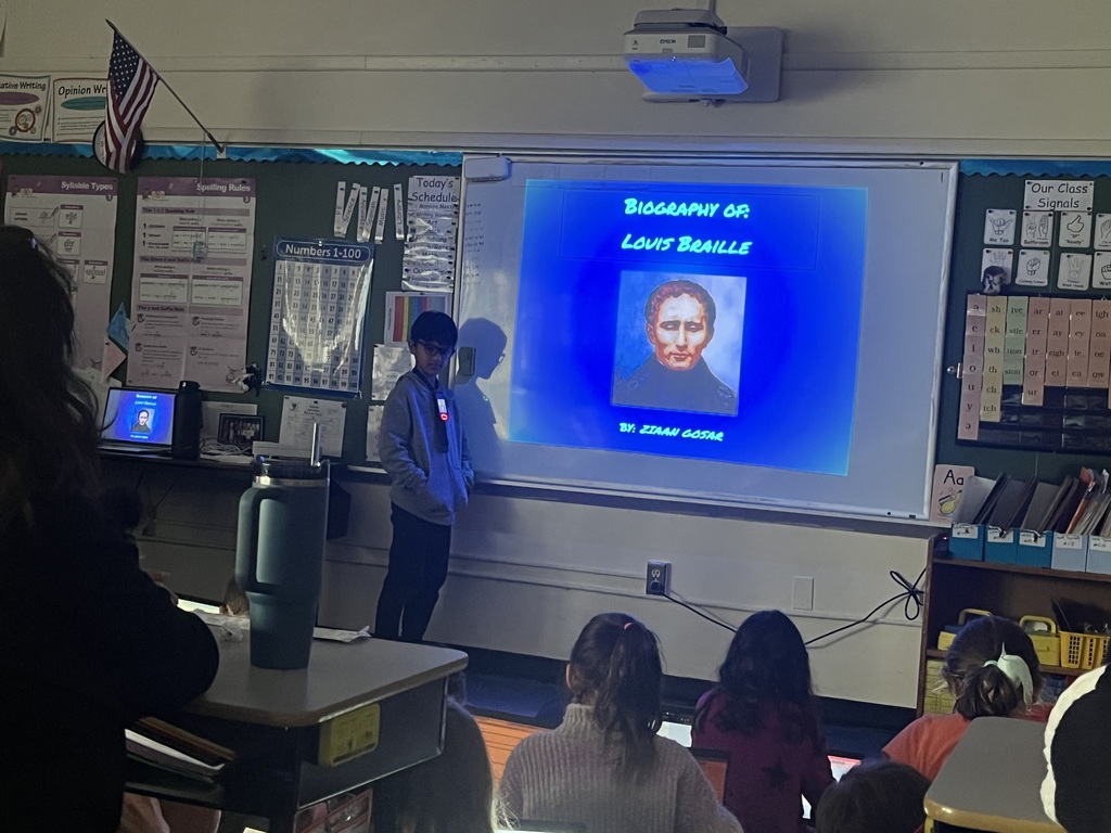 Student presents biography in front of classmates and small group of parents.