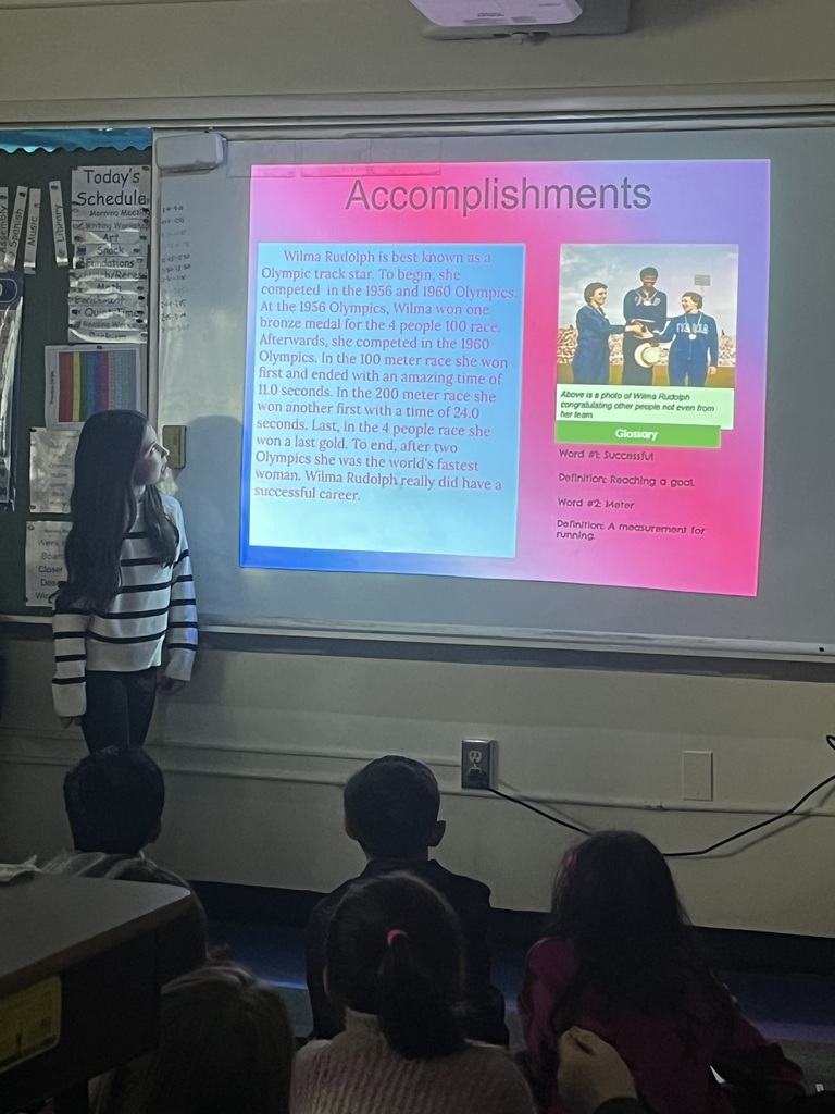 Student presents biography in front of classmates and small group of parents.