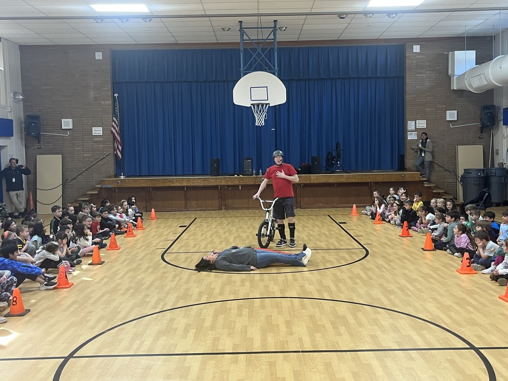 The presenter is preparing to jump over two teachers while riding his bike.