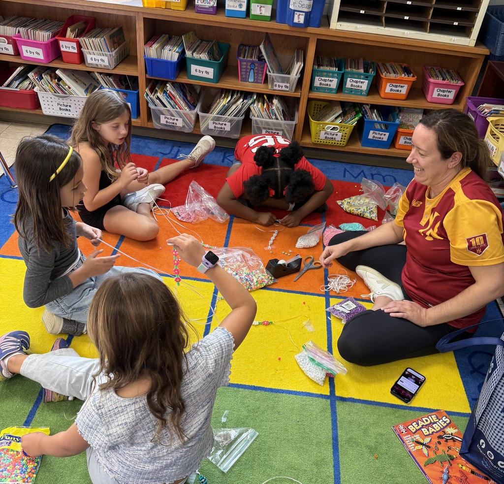 students sitting on carpet, with teacher, working on bead project