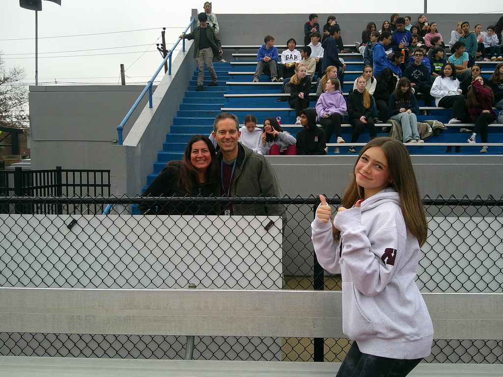student and teachers smiling in front of stand