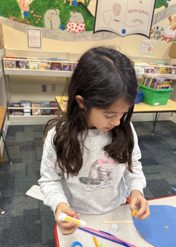 a  student sitting at a table, working on a craft at Book Club