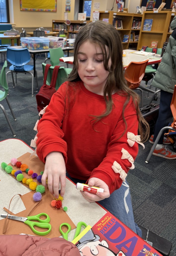 a  student sitting at a table, working on a craft at Book Club