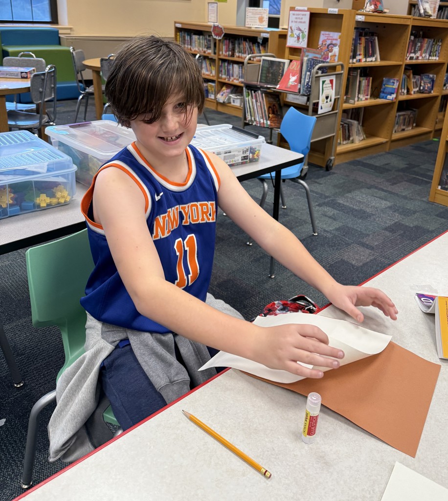 a  student sitting at a table, working on a craft at Book Club