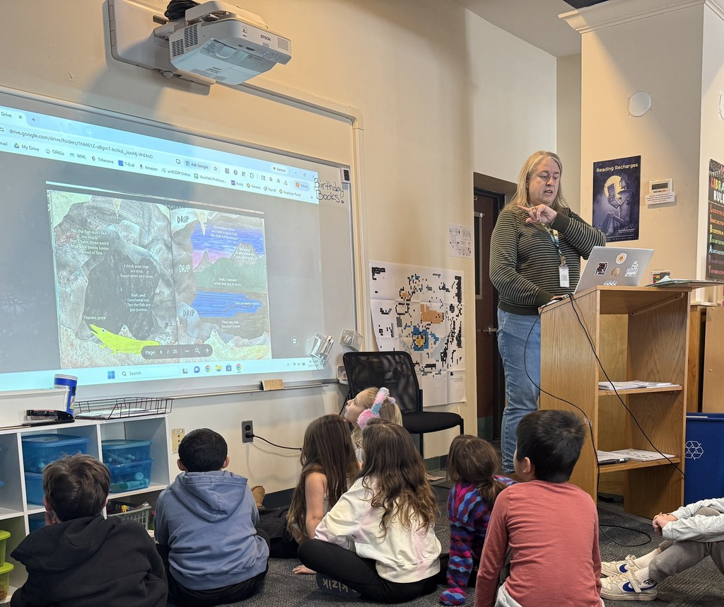 students sitting on the carpet, listening to a Caldecott book during library class