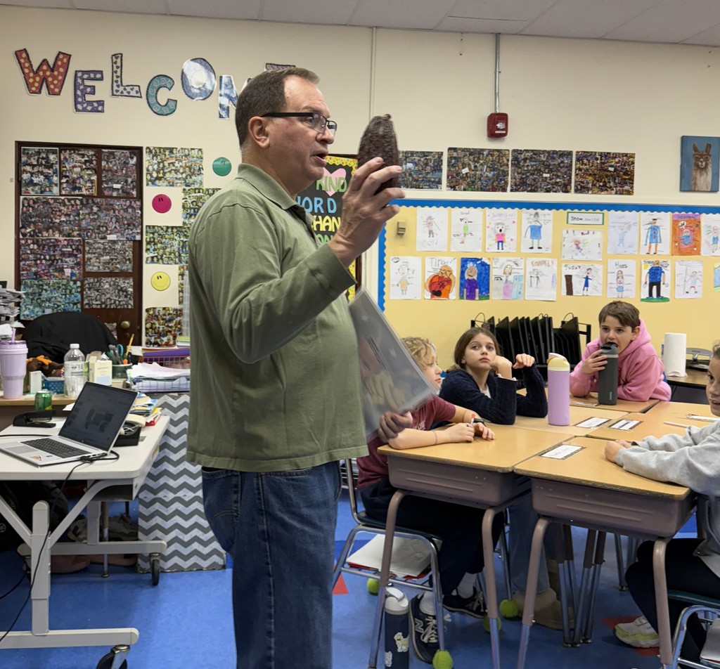 a tree steward holding a pine cone, standing in front of the class