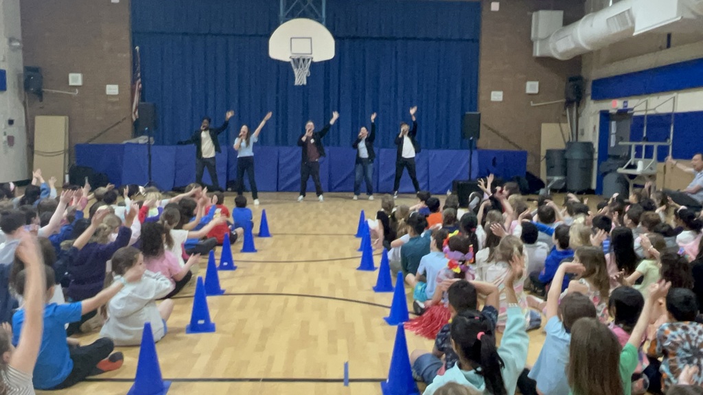 The performers are singing and dancing, while students also move their hands to the lyrics. 