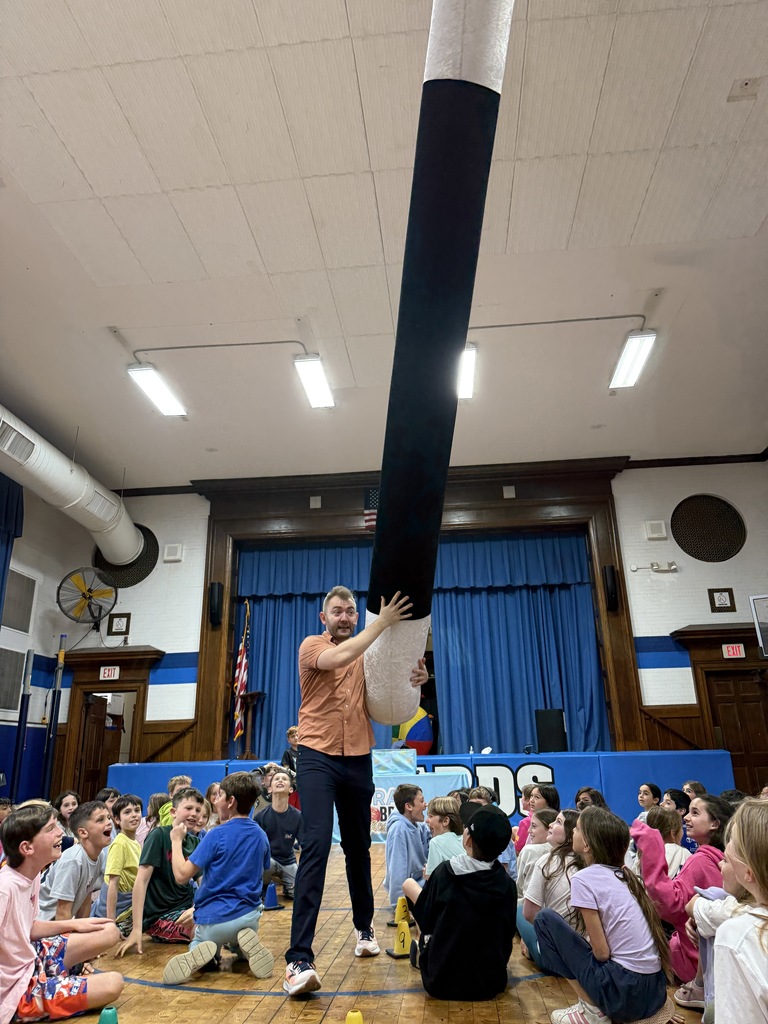 students watching Brain Break assembly presenter carry very large magic wand