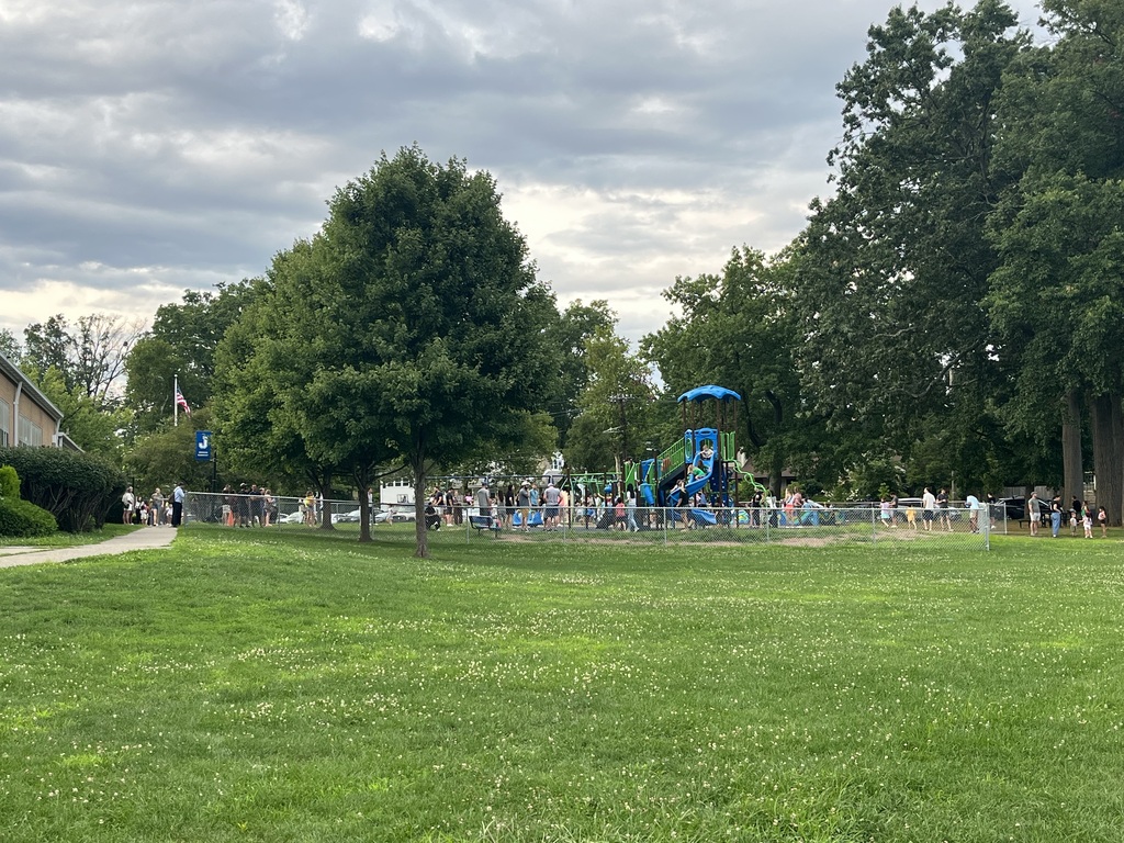 Parents mingling and students playing on the playground a beautiful evening.