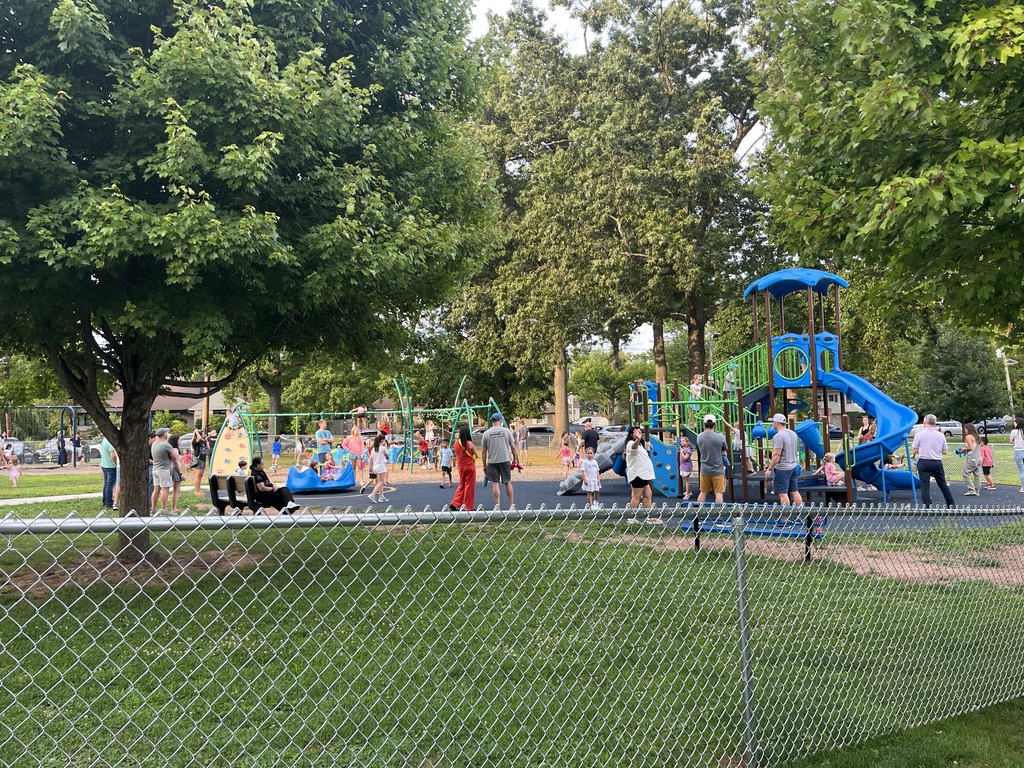 Parents mingling and students playing on the playground a beautiful evening.