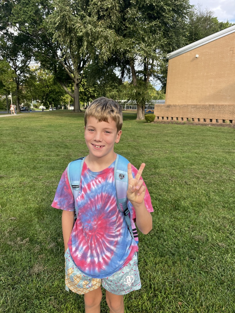 Student showing the peace sign and wearing tie dye shirt.
