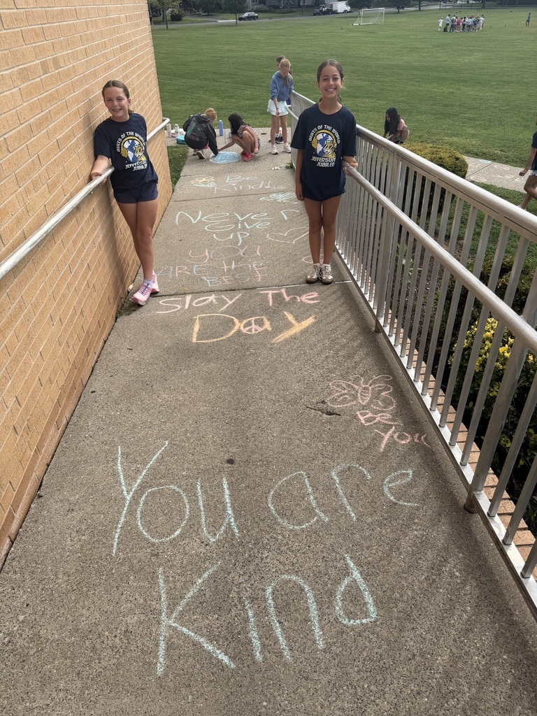 Two students stand along a concrete ramp covered in colorful sidewalk chalk messages like "You are Kind" and "Slay The Day".