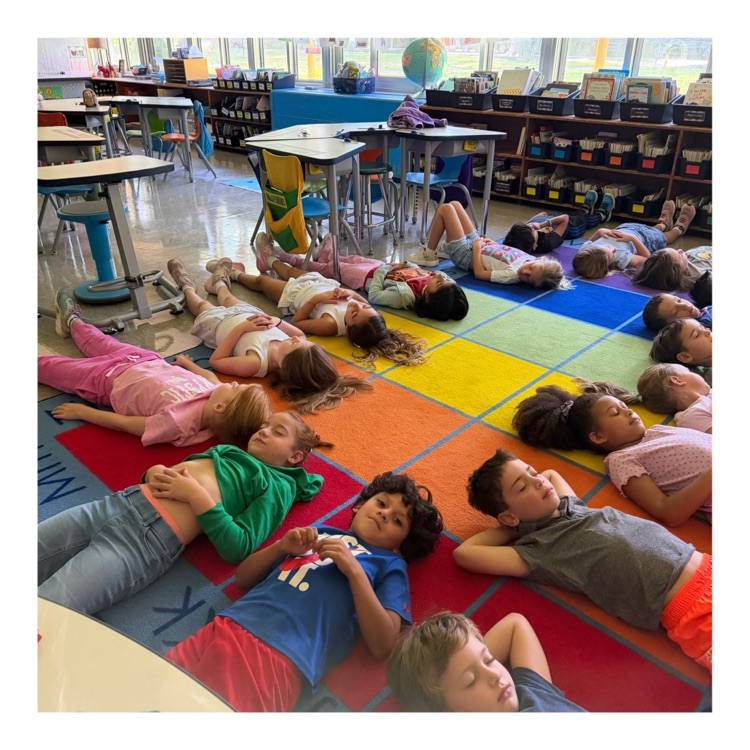 Elementary school students lie down on a vibrant, multi-colored grid rug for a quiet rest or mindfulness exercise in the classroom