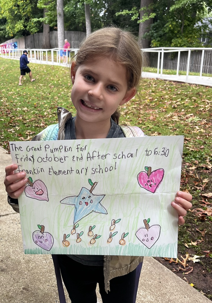 A young girl holds up a sign promoting the Great Pumpkin fair on October 2 after school to 6:30 PM at Franklin Elementary School
