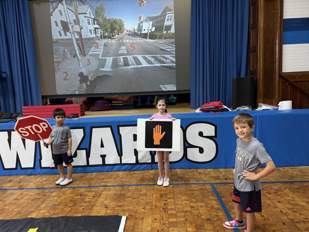 2 second grade students holding up pedestrian safety symbols and one student standing near them