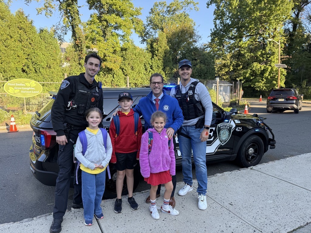 Three young students standing in front of a Westfield Police vehicle with two police officers and the principal on a sunny morning.
