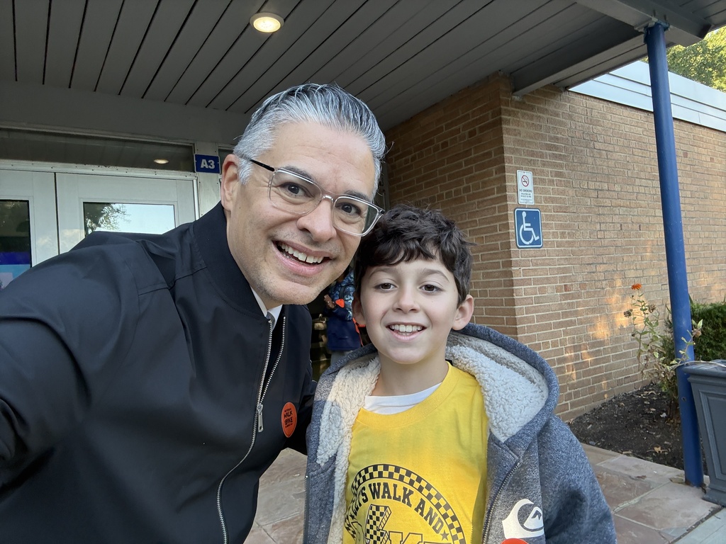 A selfie of a smiling adult man wearing glasses next to a young boy wearing a yellow t-shirt with a checkered "Walk and Bike" crest.