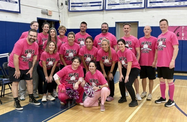 A group picture of Westfield High School staff members wearing matching pink t-shirts that read "WHS Staff vs Students 2026," posing and smiling together on the gym floor.