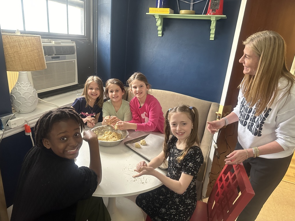 girls sitting at a table making cookies with a teacher