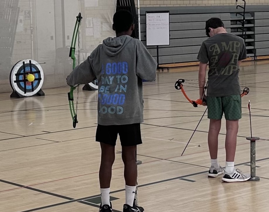 Two students with bow and arrows in front of target