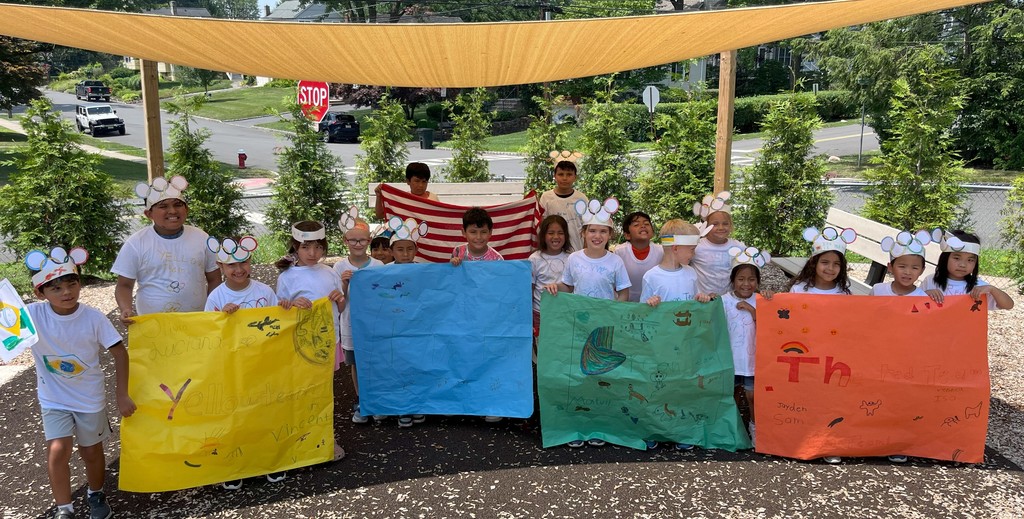 Group photo of students wearing hand made olympic hats and holding colorful signs representing their teams
