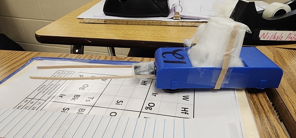 This is the Physics  Egg Lab.  Each group was tasked with the objective of protecting an egg.  So, in the middle of all that 'stuff' is an egg.  After the car traveled down a ramp that was 27 books high (about 0.92 meters) three times, I unwrapped the egg and checked for fractures.  They had a limited budget and were allowed to purchase different materials.  They were allowed to bring one item from home that fit into a 6 inch x 6 inch area.  They had 3 minutes to build their car with bumpers and protection for the egg.  They were so innovative with their materials they brought from home.  After all of this, they had to calculate speed, kinetic energy and potential energy.  This is their final lab in a series of labs where they learned how to do calculations, write labs, understand the cart and how it moved, and measurement. Warrior Work Ethic in full force!