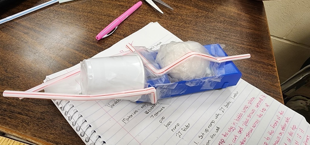This is the Physics  Egg Lab.  Each group was tasked with the objective of protecting an egg.  So, in the middle of all that 'stuff' is an egg.  After the car traveled down a ramp that was 27 books high (about 0.92 meters) three times, I unwrapped the egg and checked for fractures.  They had a limited budget and were allowed to purchase different materials.  They were allowed to bring one item from home that fit into a 6 inch x 6 inch area.  They had 3 minutes to build their car with bumpers and protection for the egg.  They were so innovative with their materials they brought from home.  After all of this, they had to calculate speed, kinetic energy and potential energy.  This is their final lab in a series of labs where they learned how to do calculations, write labs, understand the cart and how it moved, and measurement. Warrior Work Ethic in full force!