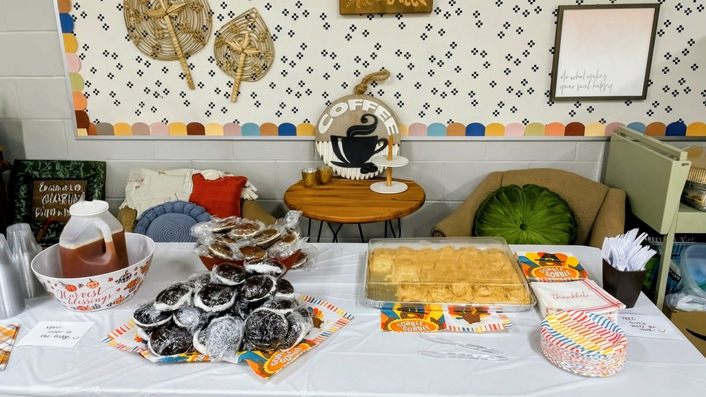 A dessert table at a fall-themed gathering, featuring plates of cookies, a large pan of baked goods, a jug of cider, and colorful fall decorations.