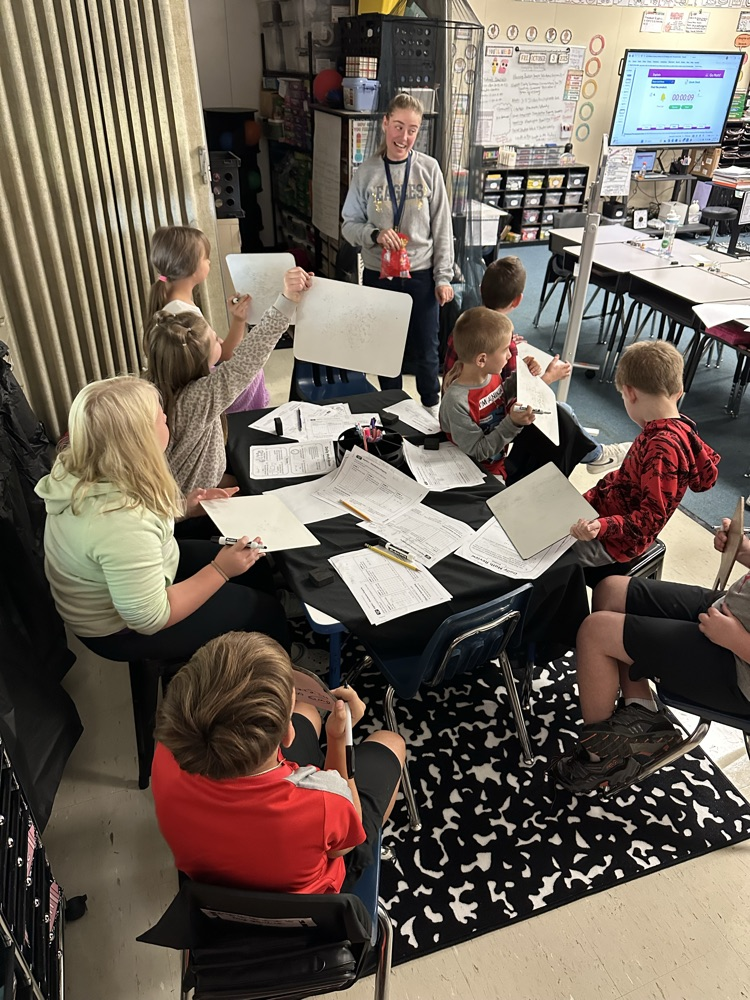 group of students around the table with whiteboards  teacher standing 