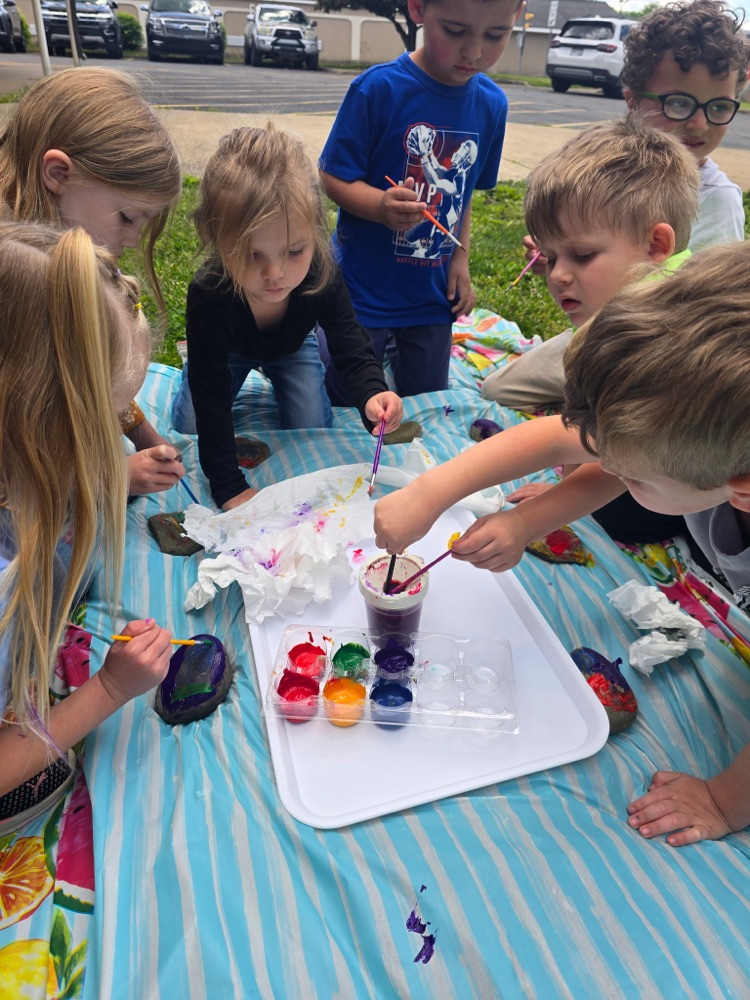 7 students painting rocks on a turquoise and white table cloth