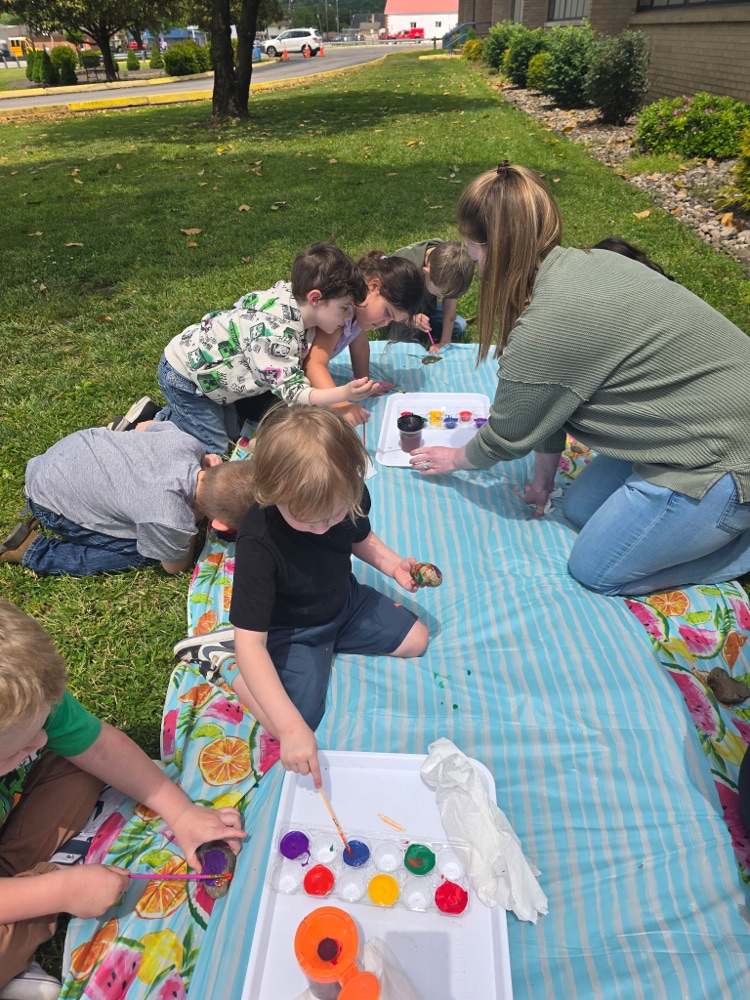 6 students painting rocks with an adult helper 