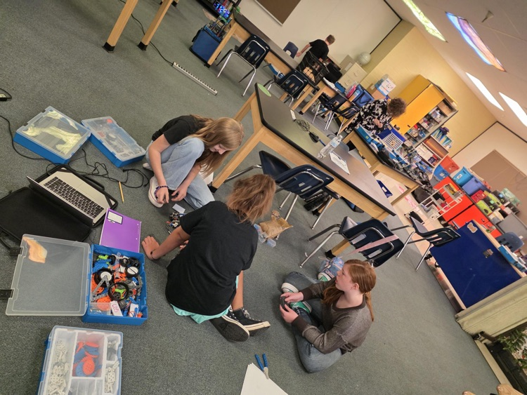 three students on floor working with a robot 