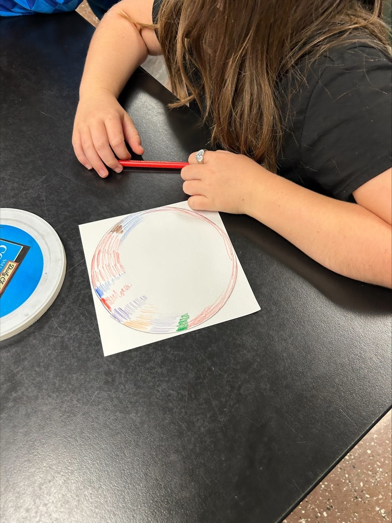 A person coloring a circle on a white sheet of paper. A black table is in the foreground.