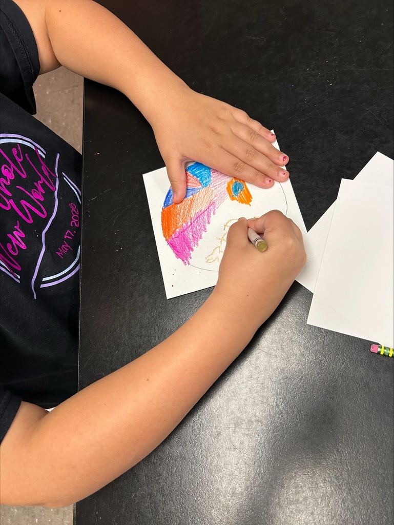 A person in a black shirt draws a colorful circle on a paper at a table.