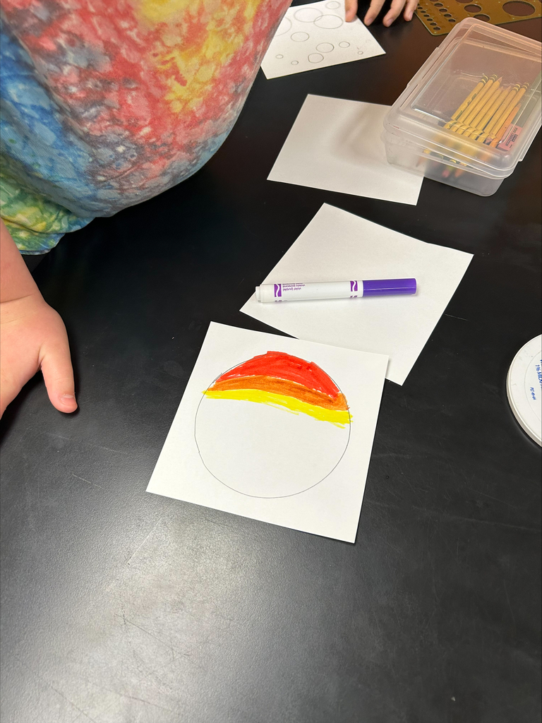 Person at a desk with colored pencils and papers. A circle is colored in red, orange, and yellow.
