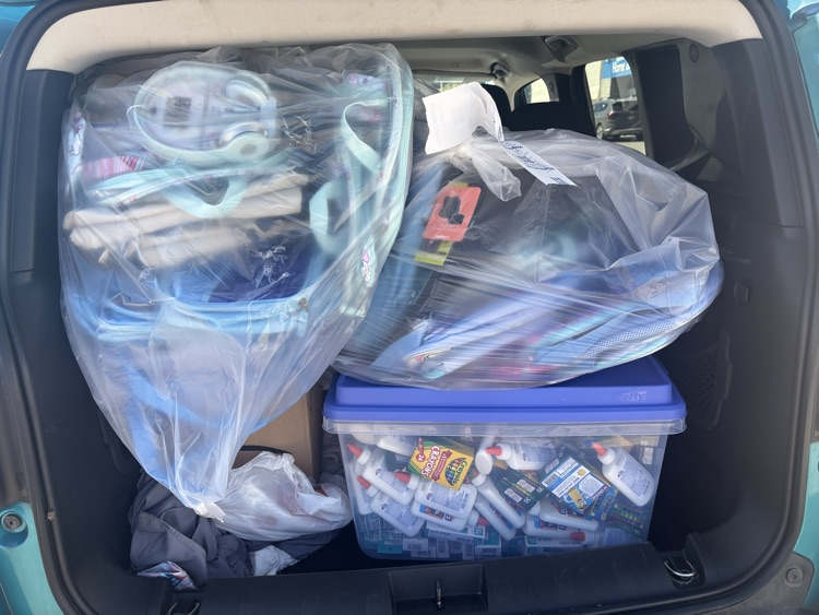 a tote and garbage bags full of backpacks, crayons, glue and other supplies. 