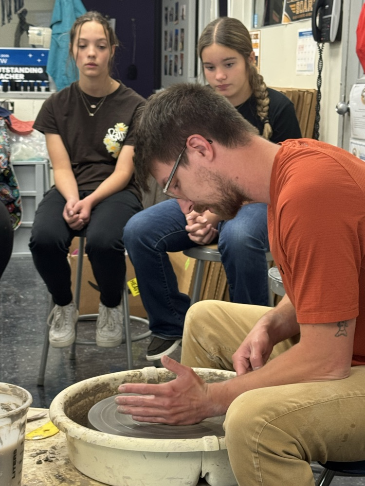 Jake Pierce demonstrates how to use the pottery wheel to a group of students. 
