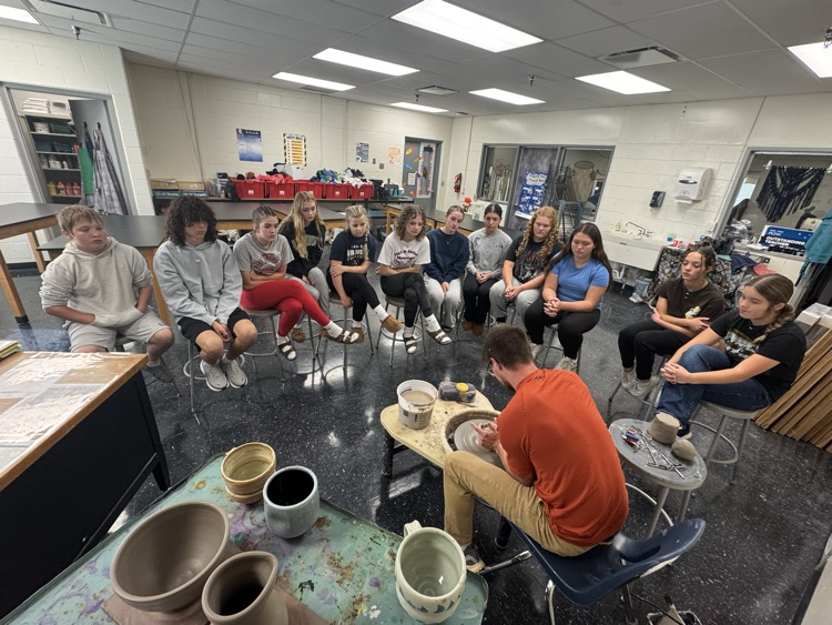 Jake Pierce demonstrates how to use the pottery wheel to a group of students. 