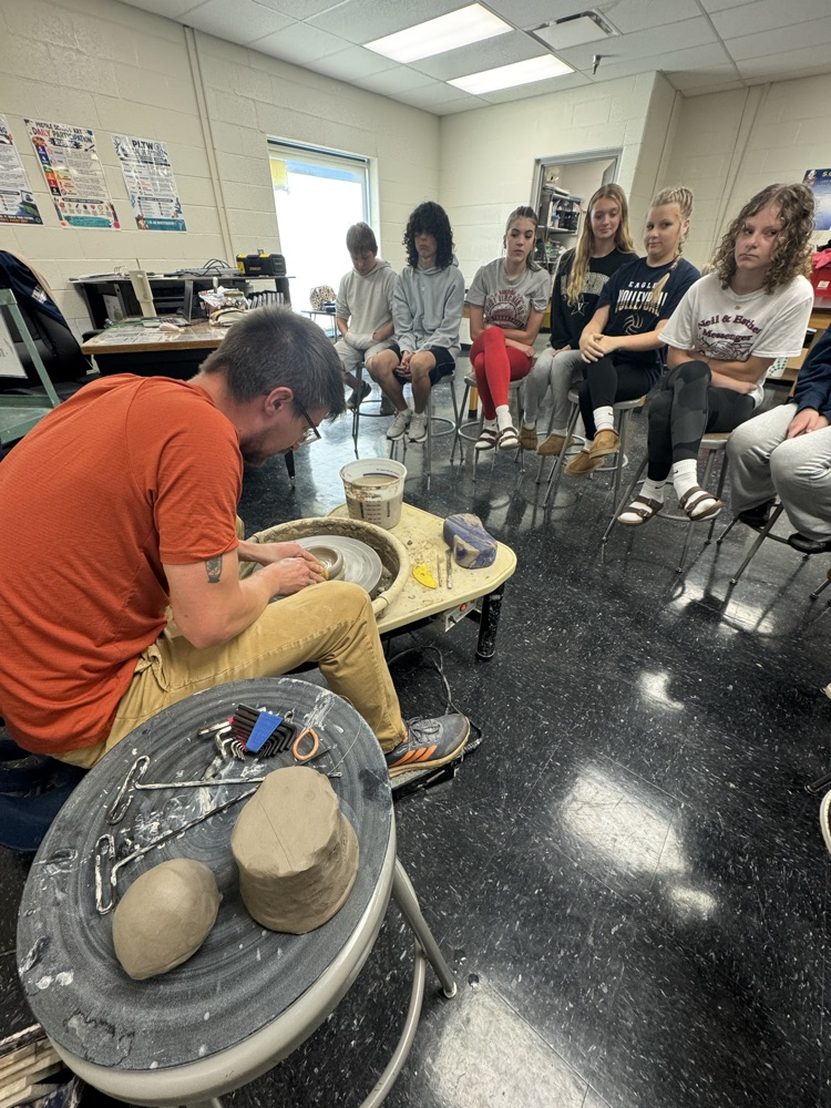 Jake Pierce demonstrates how to use the pottery wheel to a group of students. 