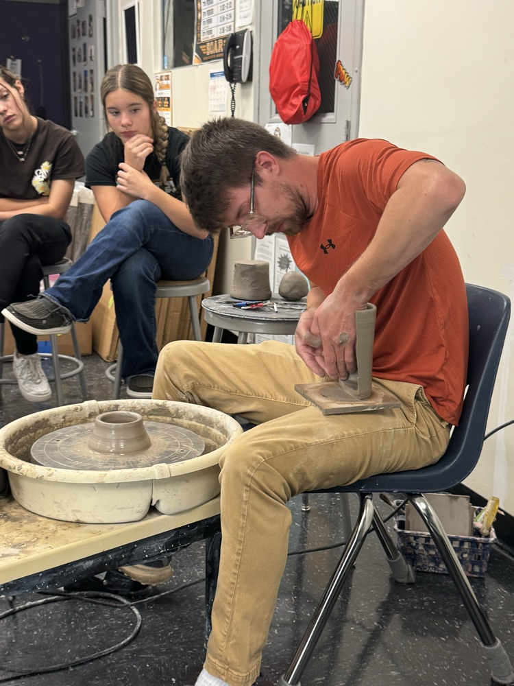 Jake Pierce demonstrates how to use the pottery wheel to a group of students. 