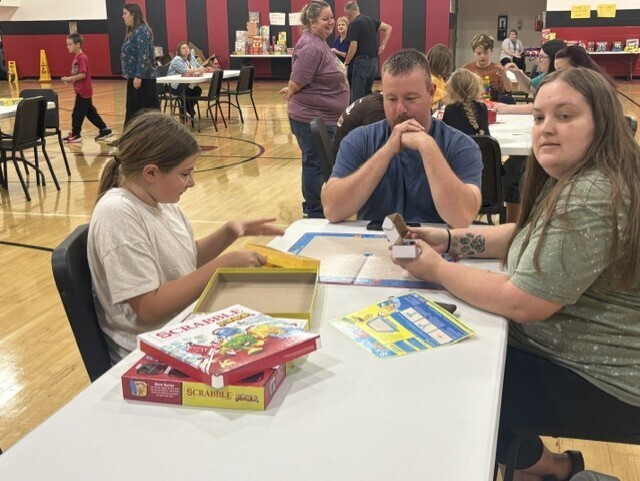 In a gym, two women and a man sit around a table. They interact with each other and play board games.