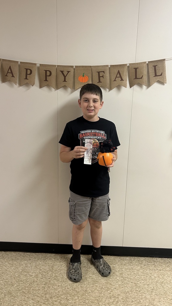 Boy holding a ticket and a pumpkin, standing in front of a white wall with a banner reading "Happy Fall."