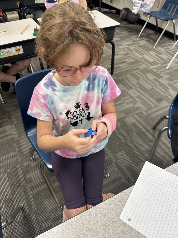 A student stands and examines a toy while a white paper rests on a table.